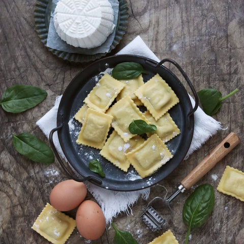 Foto dall'alto con ravioli al centro e di contorno ricotta intera, foglie di basilico e uova